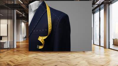 Semi-ready jacket with tailor's measuring tape on mannequin against grey background, closeup. Space for text Wall mural