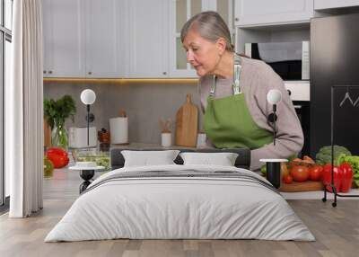 Senior woman cooking by recipe book in kitchen Wall mural