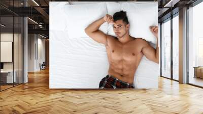 Sexy young man lying on bed with soft pillows at home, top view Wall mural