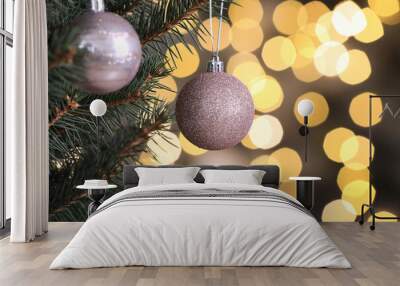 Shiny pink balls hanging on Christmas tree against festive lights, closeup Wall mural