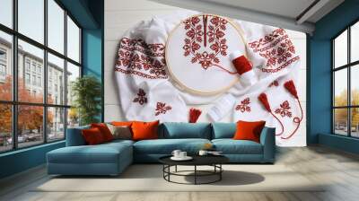 Shirt with red embroidery design in hoop, needle and threads on wooden table, flat lay. National Ukrainian clothes Wall mural