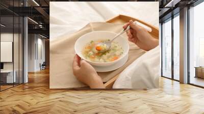 Sick woman eating fresh homemade soup to cure flu in bed at home, closeup Wall mural