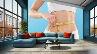 Slim woman measuring waist with tape on light blue background, closeup. Weight loss Wall mural