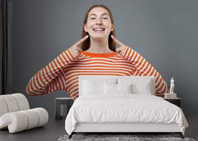 Smiling girl pointing at her braces on grey background Wall mural