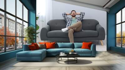 Smiling man with hands behind his head relaxing on sofa at home Wall mural