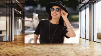 Smiling woman in stylish black hat and sunglasses outdoors Wall mural