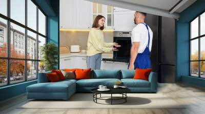 Smiling woman talking with repairman near oven in kitchen Wall mural