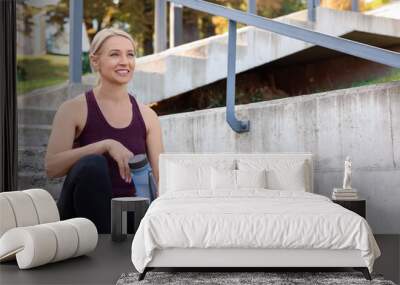 Smiling woman with bottle of water on steps outdoors Wall mural