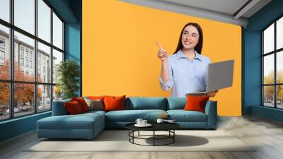 Smiling young woman with laptop on yellow background, space for text Wall mural