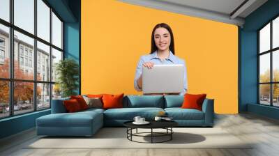 Smiling young woman with laptop on yellow background Wall mural