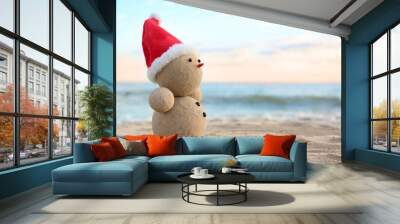 Snowman made of sand with Santa hat on beach near sea, space for text. Christmas vacation Wall mural