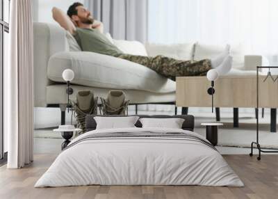 Soldier relaxing on sofa in living room, focus on pair of combat boots. Military service Wall mural