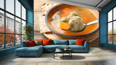 Spoon with matzoh ball over bowl of soup on table, closeup. Jewish cuisine Wall mural