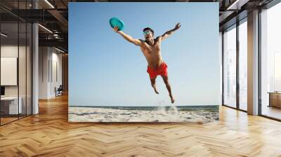 Sportive man jumping and catching flying disk at beach Wall mural