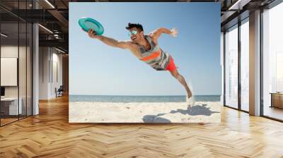 Sportive man jumping and catching flying disk at beach Wall mural