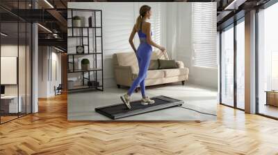 Sporty woman training on walking treadmill at home Wall mural