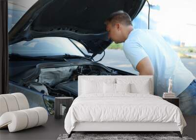 Stressed man looking under hood of broken car outdoors Wall mural