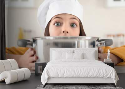 Surprised little girl wearing chef hat with pot in kitchen Wall mural