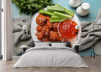 Tasty cauliflower buffalo wings, sauce and celery on light blue wooden table, flat lay Wall mural