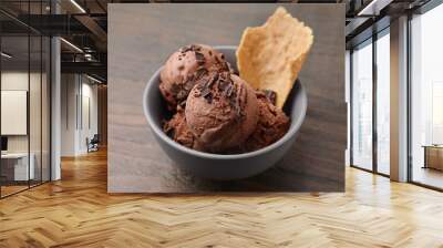 Tasty chocolate ice cream and piece of waffle cone in bowl on wooden table, closeup Wall mural