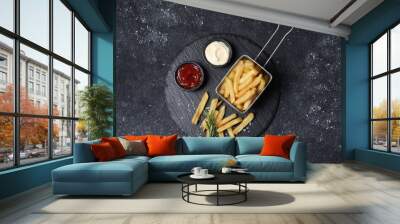 Tasty French fries, ketchup, rosemary and mayonnaise on black textured table, top view Wall mural