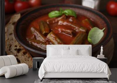 Tasty stew with okra, tomato sauce, bread and basil on wooden table, closeup Wall mural