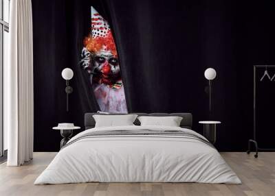 Terrifying clown hiding behind black curtains, space for text. Halloween party costume Wall mural