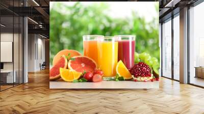 Three glasses with different juices and fresh fruits on table against blurred background Wall mural