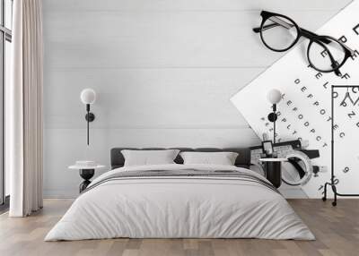 Trial frame, eye chart test, glasses and space for text on white wooden table. Ophthalmologist tools Wall mural