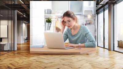 Troubled young woman working on laptop at home Wall mural