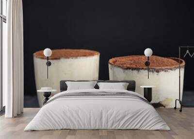 Two glasses of tiramisu cake on table against dark background Wall mural