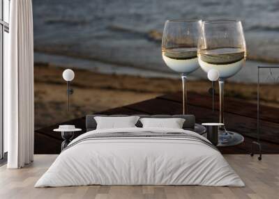 Two glasses of wine on wooden table near river at sunset. Space for text Wall mural