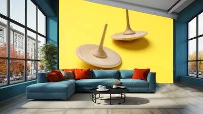 Two wooden spinning tops on yellow background, closeup Wall mural