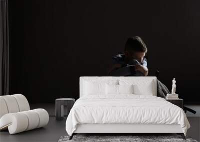 Upset boy with backpack sitting in dark room. Space for text Wall mural