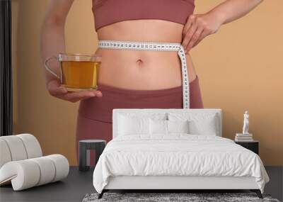 Weight loss concept. Woman with cup of diet tea and measuring tape on beige background, closeup Wall mural