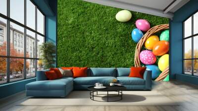 Wicker basket with Easter eggs on green grass, flat lay. Space for text Wall mural