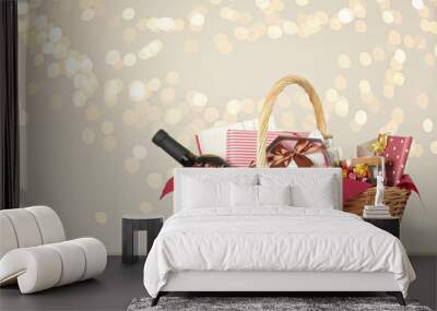 Wicker basket with gifts, wine and food against blurred festive lights. Space for text Wall mural