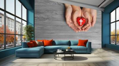 Woman and child holding heart with cross symbol on grey wooden background, top view with space for text. Christian religion Wall mural