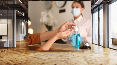 Woman applying antiseptic gel at hotel reception, closeup Wall mural