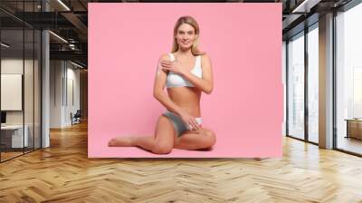 Woman applying body cream onto her arm against pink background Wall mural