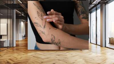 Woman applying cream on her arm with tattoos against light background, closeup Wall mural