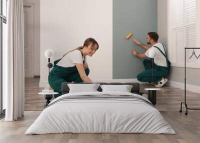 Woman applying glue onto wall paper while man hanging sheet indoors Wall mural