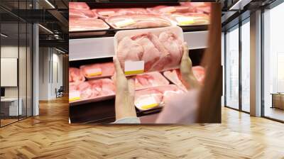 Woman choosing packed chicken meat in supermarket Wall mural