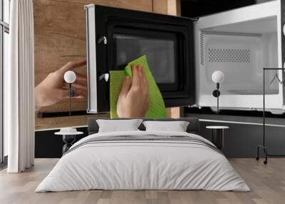 Woman cleaning microwave oven with rag in kitchen, closeup Wall mural