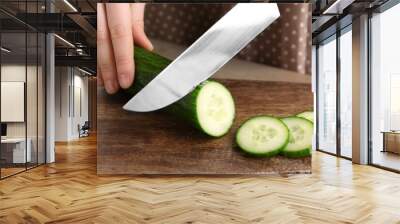 Woman cutting cucumber on wooden board, closeup Wall mural