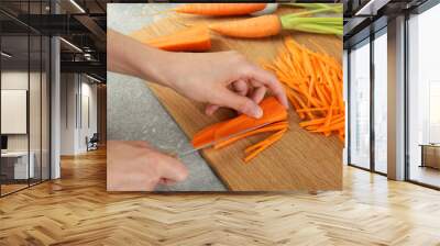 Woman cutting fresh carrot at gray textured table, closeup Wall mural