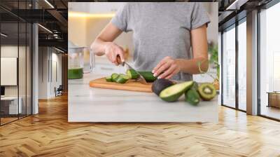 Woman cutting fresh cucumber at white marble table in kitchen, closeup Wall mural