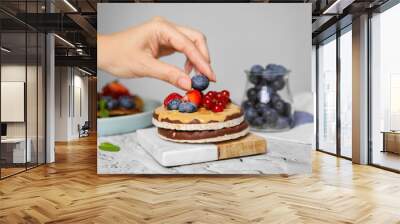 Woman decorating crunchy rice cakes with blueberry at white textured table, closeup Wall mural