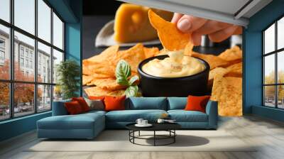 Woman dipping crispy nacho into delicious cheese sauce at table, closeup Wall mural