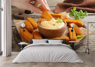 Woman dipping delicious chicken nuggets into cheese sauce at wooden table, closeup Wall mural